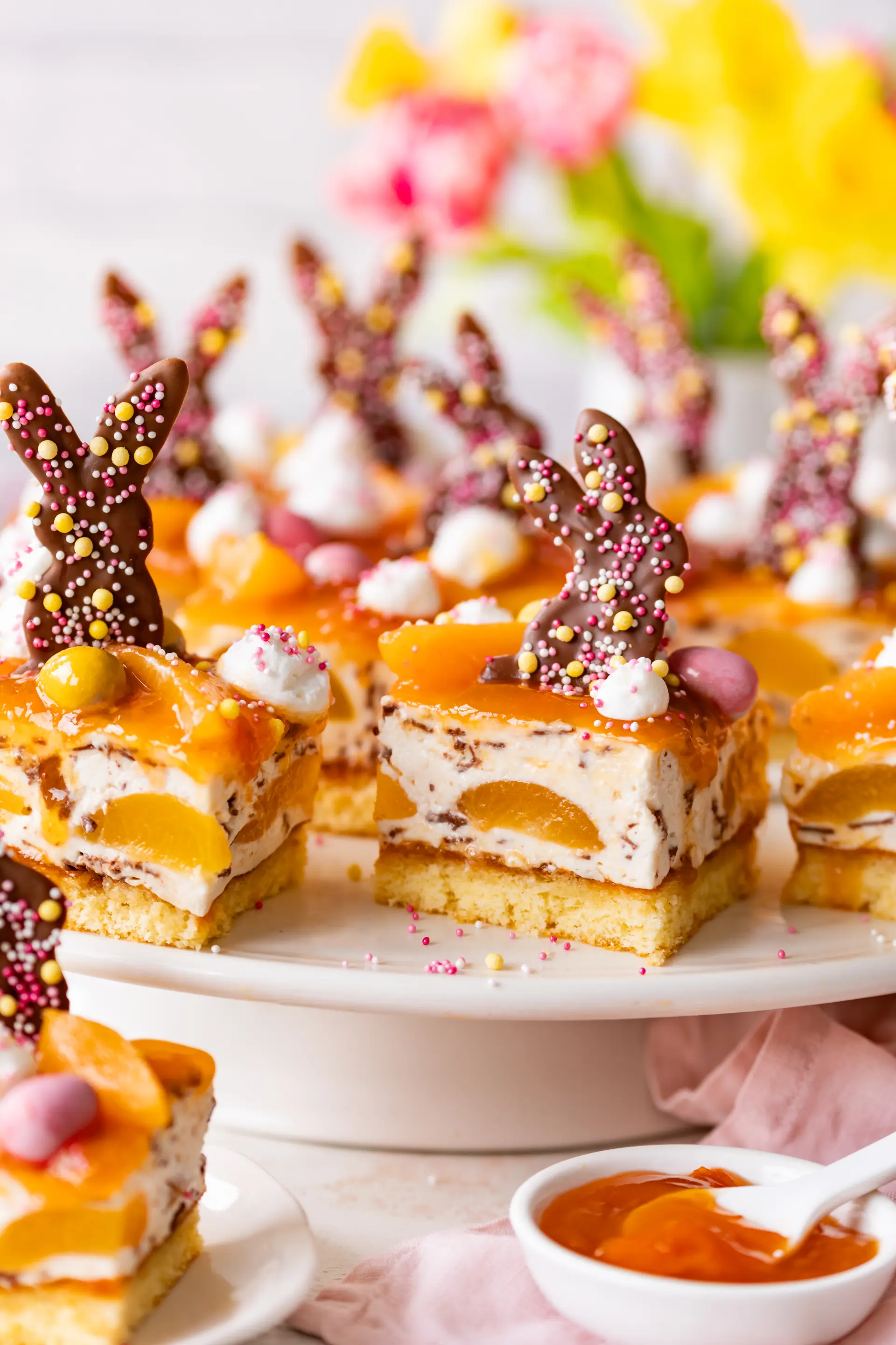 Blechkuchen mit Aprikosen und Stracciatella-Creme, dekoriert mit Schokohasen und Streuseln auf einer Tortenplatte.
