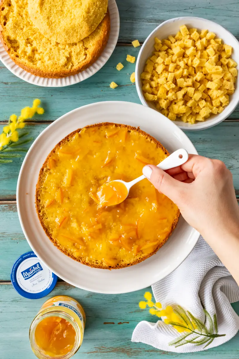 Torta Mimosa mit Zitronencreme und Orangen-Marmelade Der untereste Boden der Torta Mimosa wird mit Orangen-Marmelade bestrichen.