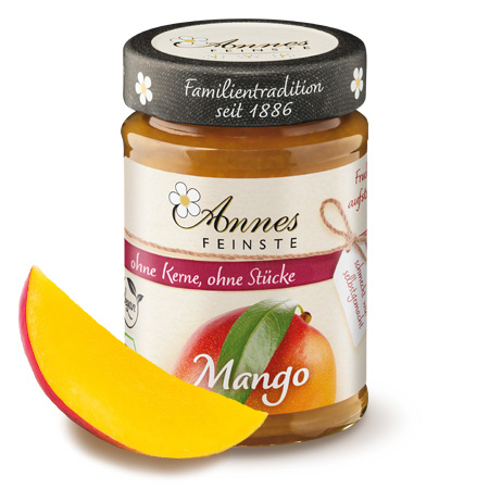 Annes Feinste Bio Mango Fruchtaufstrich, fein passiert Glas Annes Feinste Bio Mango Fruchtaufstrich, fein passiert, daneben ein Mangostück.