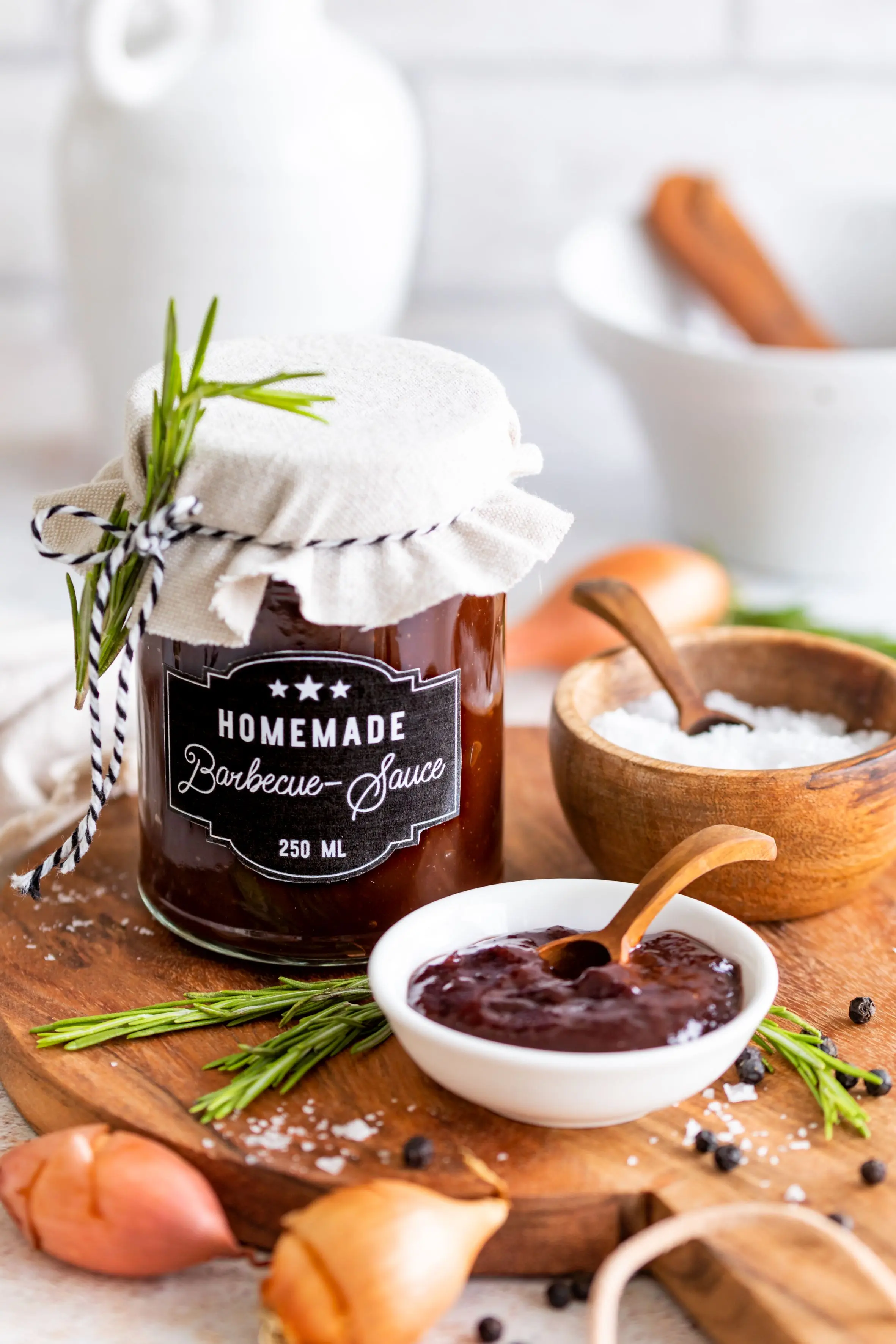 Fruchtig-würzige Barbecue-Sauce mit Hagebutten-Konfitüre Glas mit hausgemachter Barbecue-Sauce, daneben Schale mit Dip, Kräuter, Salz und Gewürze auf Holzbrett