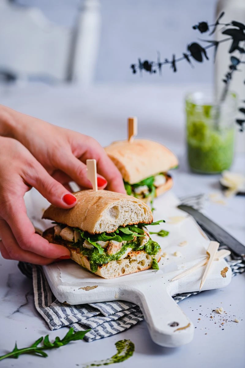 Ein gegrilltes Hähnchen Sandwich mit Pesto wird von der Servierplatte genommen.