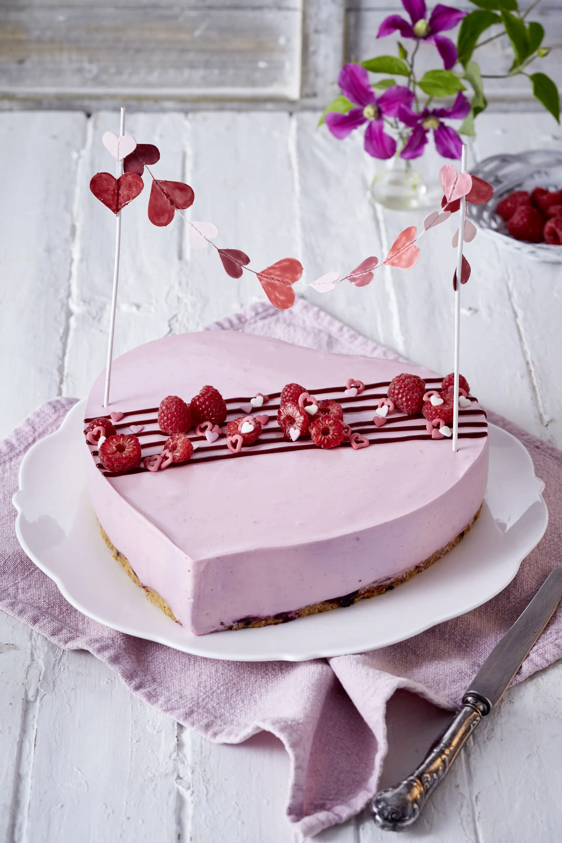 Herzförmige Himbeer-Quarktorte für Muttertag Herzförmige rosa Torte mit Himbeeren und Herzgirlande