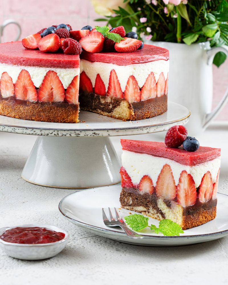 Rotkäppchen-Torte mit Erdbeeren auf Tortenplatte, davor ein Stück auf Teller und Schüssel mit Aufstrich.