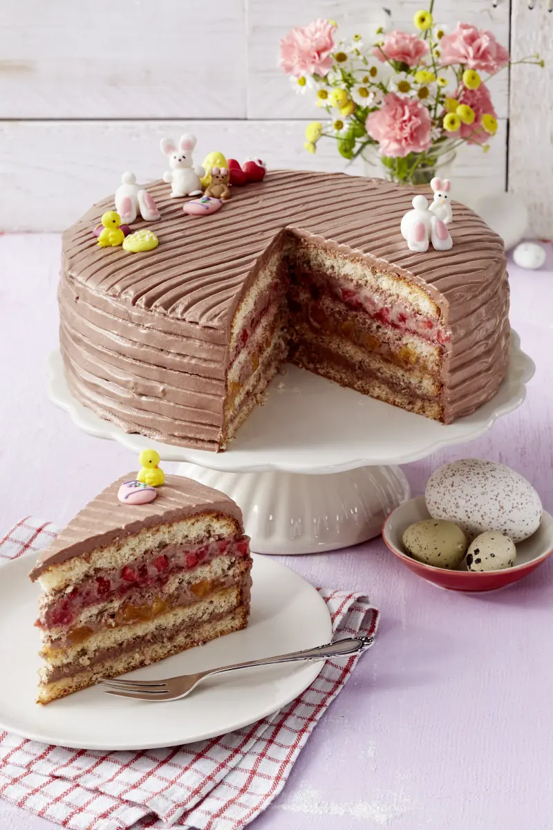 Ostertorte mit Schoko-Creme und Frucht Ostertorte mit Schokocreme, Frucht und Osterdeko auf Platte, davor Tortestück auf Teller.
