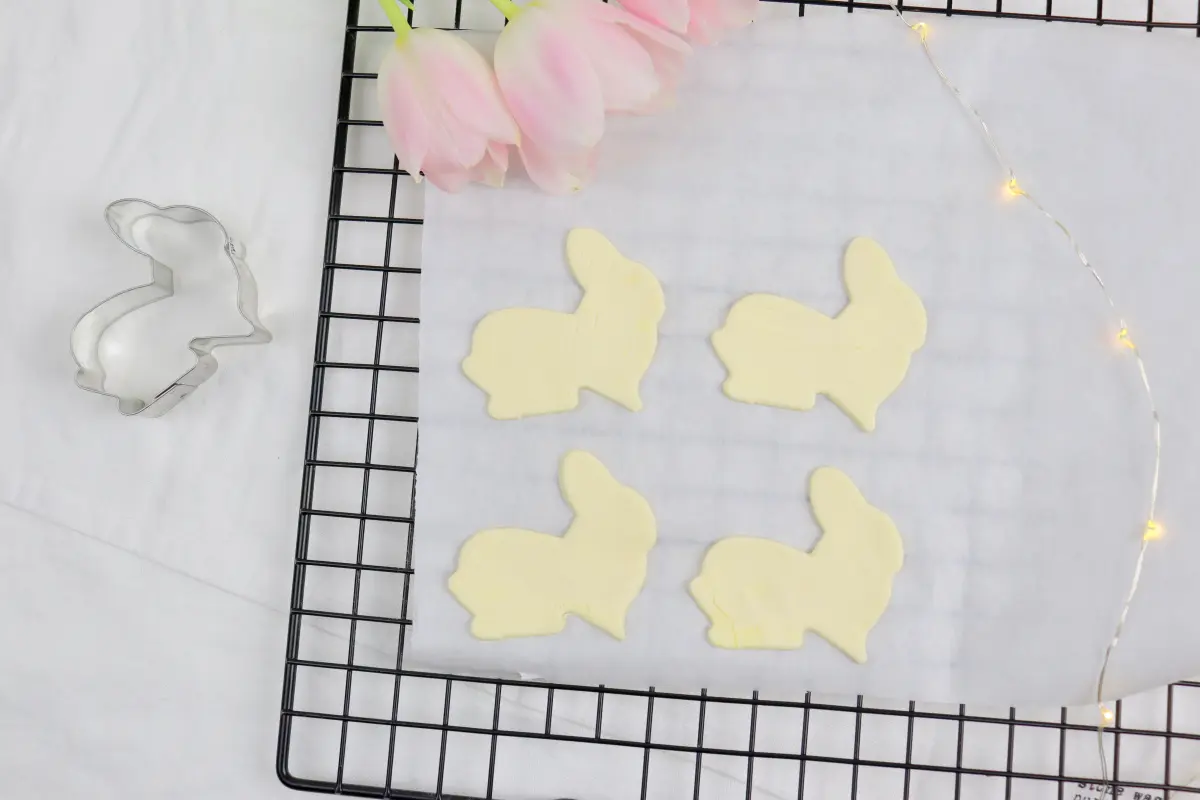 Gefüllte Blätterteig-Osterhasen mit Buttercreme und Hagebuttenfüllung Ausgestochene Blätterteighasen, ungebacken, liegen auf Gitterrost mit Backpapier.