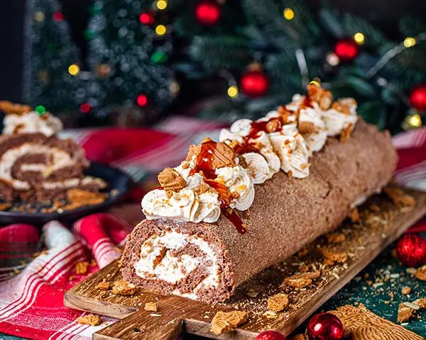 Spekulatius-Biskuitrolle mit Frischkäse-Sahne-Creme Spekulatius-Biskuitrolle auf Holzbrett serviert. .