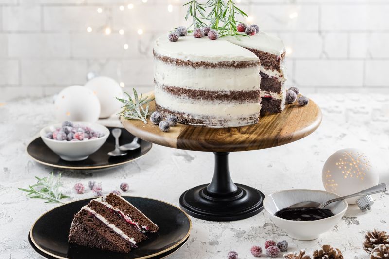Winterlicher Naked Cake mit Waldfrucht-Fruchtaufstrich auf hoher Tortenplatte, daneben ein Stück auf einem Teller, Schüssel mit Aufstrich und Löffel.
