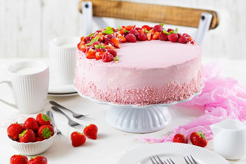 Windbeuteltorte mit Gartenfrüchten Kaffeetafel mit Windbeuteltorte mit Gartenfrüchten auf Tortenplatte, Teller, Kaffeetassen und Schüssel mit frischen Erdbeeren.