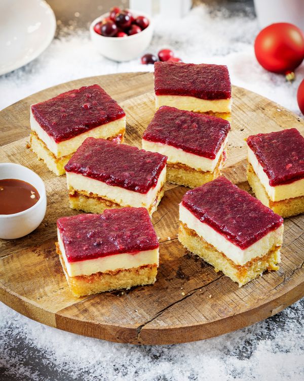 Winterlicher Blechkuchen mit Preiselbeer-Glühweinspiegel In Stuecke geschnittener Blechkuchen mit Preiselbeer-Gluehweinspiegel auf einer Holzplatte.