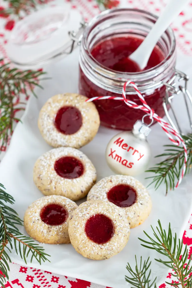 Huserenplätzchen auf Servierplatte mit Glas mit Konfitüre und Löffel, sowie Weihnachtskugel mit Merry Xmas.