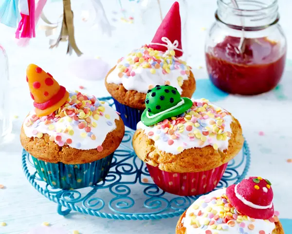 Hagebuttenmuffins mit weißem Guss, Zuckerstreuseln und kleinen Partyhüten als Dekoration.