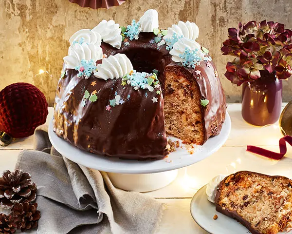 Dekorierter Tisch mit einem angeschnittenen Haselnuss-Hagebutten-Marmorkuchen auf Tortenplatte.