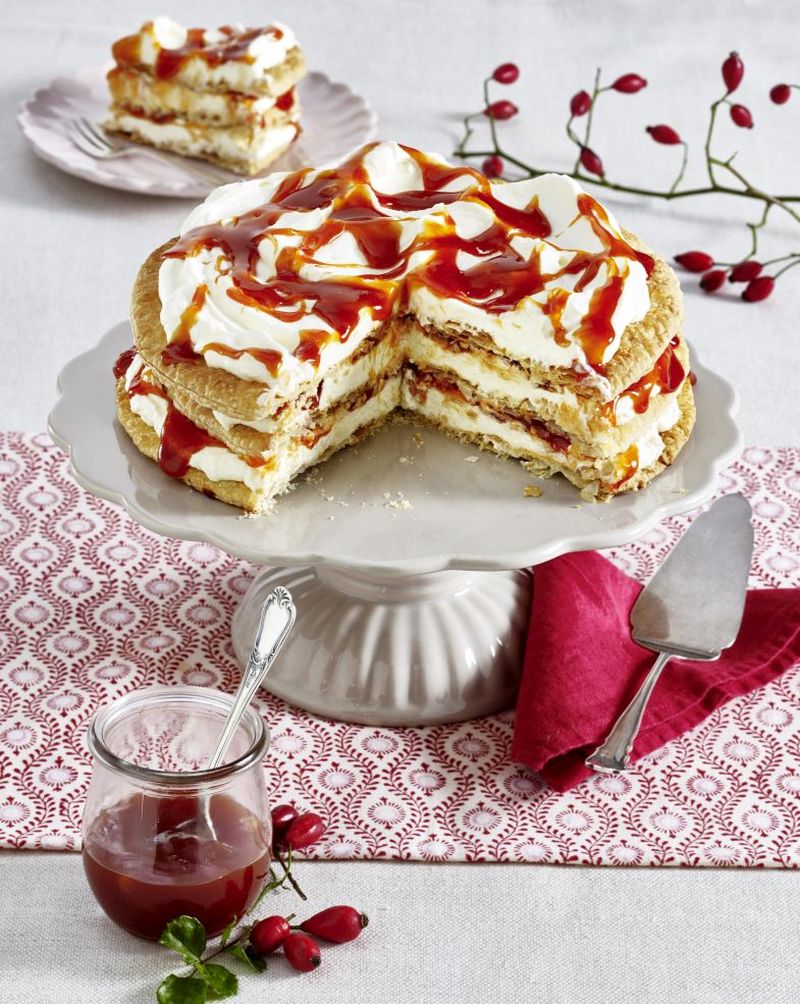 Hagebutten-Sahne-Torte mit Blätterteig Hagebutten-Sahne-Torte mit Blätterteig auf Tortenplatte, Im Vordergrund steht ein Glas mit Hagebutten-Konfitüre, im Hintergrund ein Stück auf Teller.