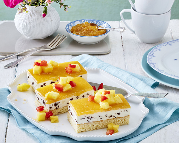 Blechkuchen mit Stracciatellacreme und Aprikosentopping Gedeckte Kaffeetafel mit Blechkuchen mit Stracciatellacreme und Aprikosentopping auf Torteplatte.
