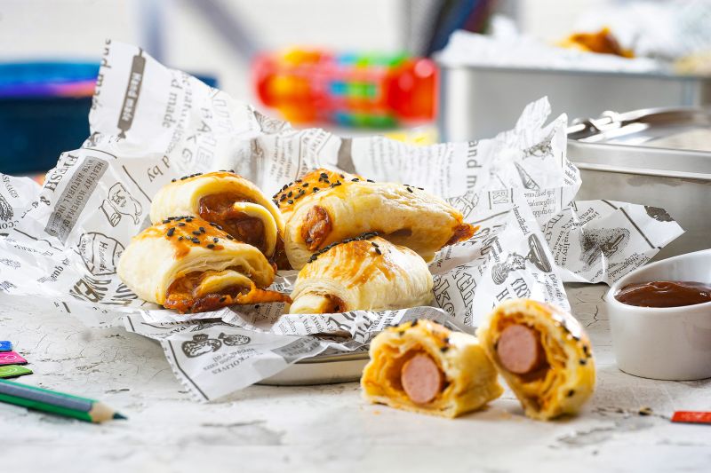 Würstchen im Schlafrock mit Johannisbeeren – BBQ-Sauce Würstchen im Schlafrock auf Papier und Teller auf einem Schreibtisch.