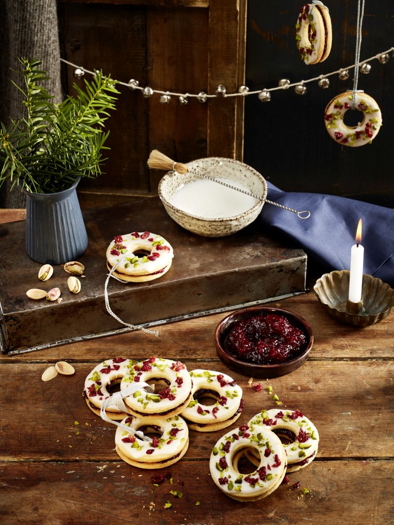 Cranberry-Adventskringel Mehrere Cranberry-Adventskringel auf Holzbrett. Daneben Schüsselchen mit Cranberry-Konfitüre, eine mit Puderzucker, Kerze, Vase mit Zweigen.