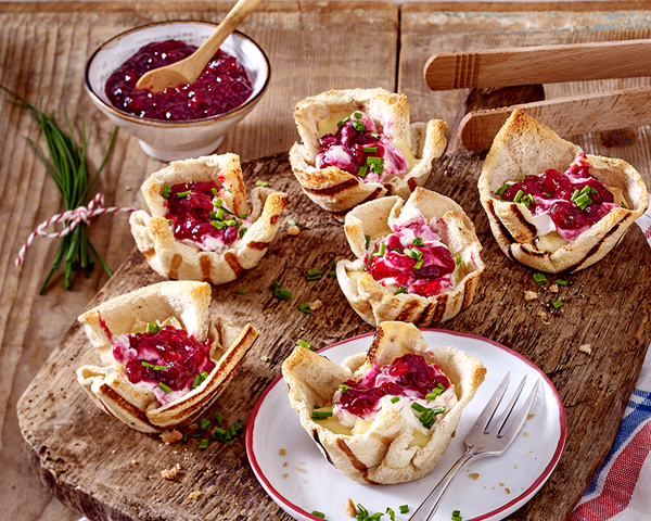 Wild-Preiselbeeren Auslese Serviervorschlag: Gegrillte Toastkoerbchen, gefuellt mit Camembert und Preiselbeeren auf Holzbrett und Schüssel mit Preiselbeeren.