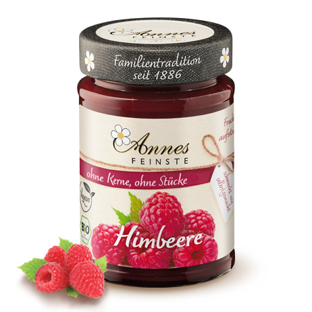 Annes Feinste Bio Himbeer-Fruchtaufstrich, fein passiert Glas Annes Feinste Bio Himbeer-Fruchtaufstrich, fein passiert, daneben Himbeeren.