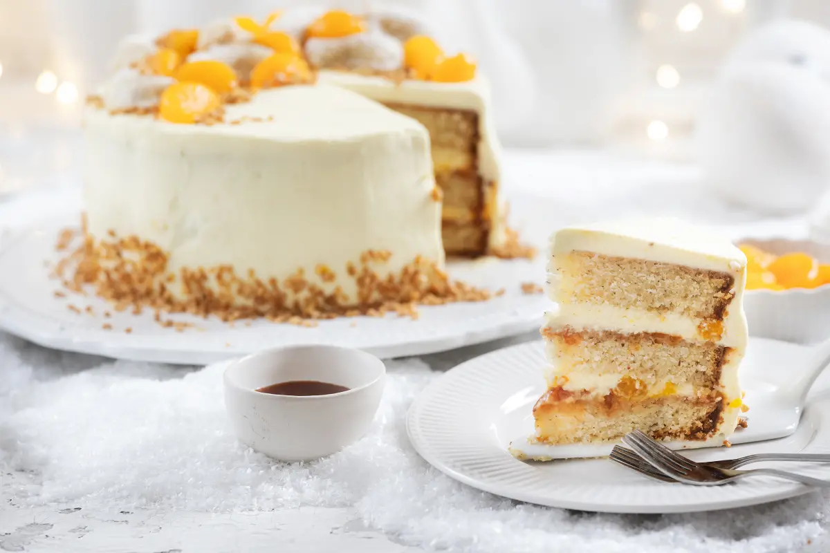 Vanillekipferltorte mit einer Mandarinen-Sahnecreme und Hagebutten-Konfitüre Vanillekipferltorte mit einer Mandarinen-Sahnecreme und Hagebutten-Konfitüre auf Tortenplatte, ein Stück davon auf einem Teller mit Besteck davor.