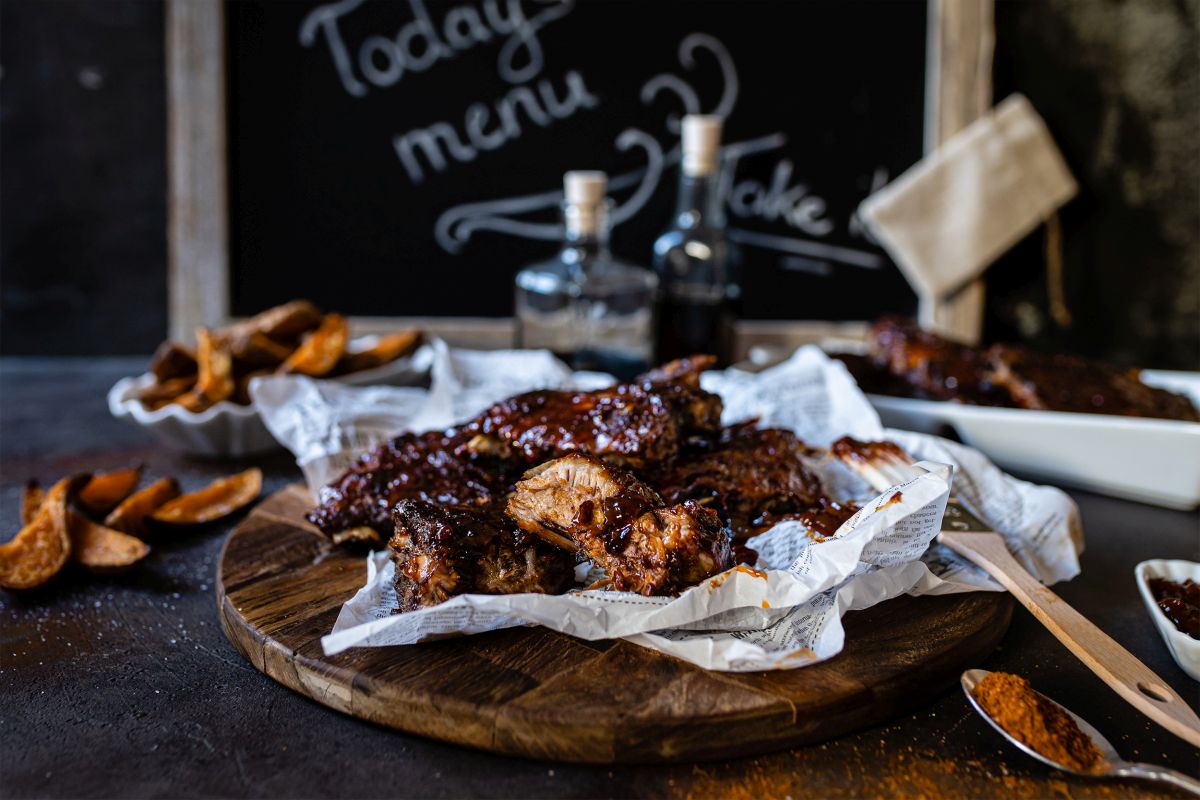 Spareribs aus dem Ofen mit Hagebutten-Barbecuesauce auf Backpapier und Holzteller.