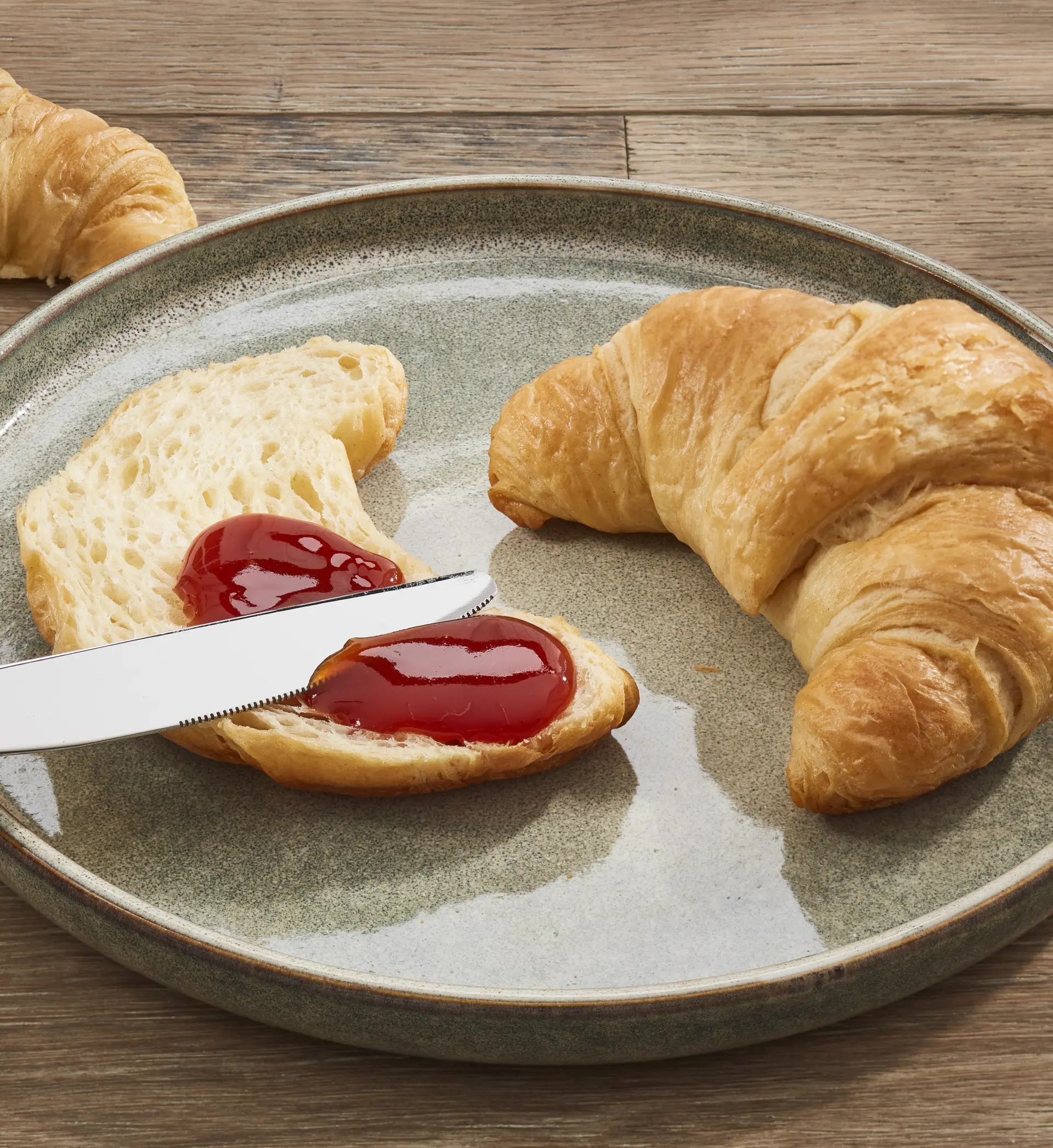 Aufgeschnittenes Croissant mit roter Hagebutten-Konfitüre auf einem Teller, daneben ein weiteres Croissant.