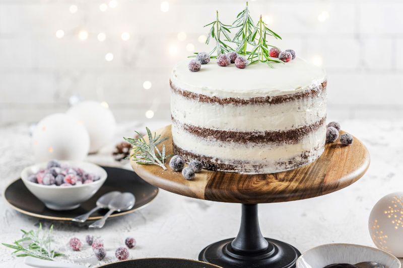 Winterlicher Naked Cake mit Waldfrucht-Fruchtaufstrich auf hoher Tortenplatte, Teller und Schüssel mit Früchten und zwei Löffel.