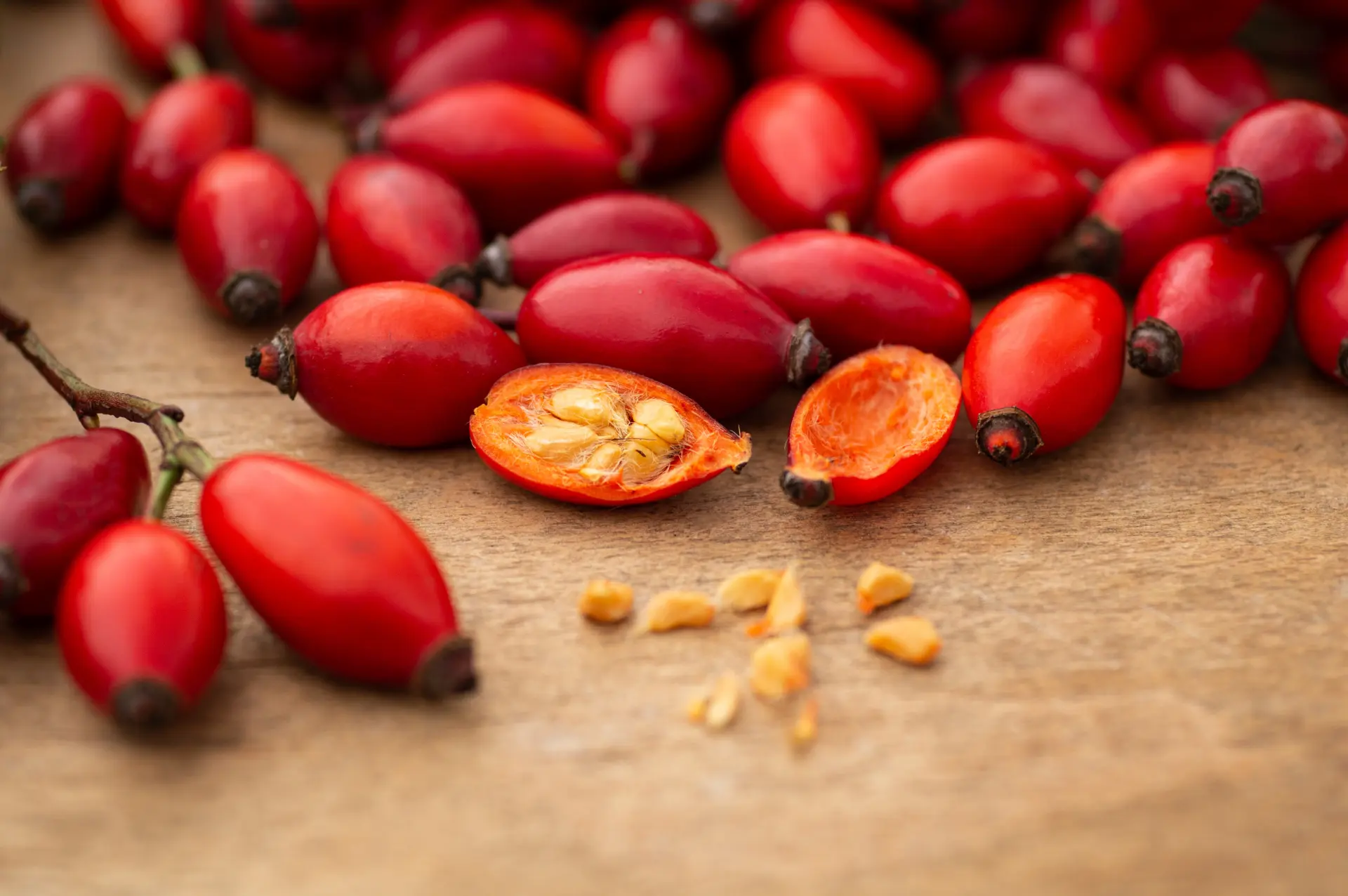 Rote Hagebutten auf einer Holzfläche, eine Frucht ist aufgeschnitten und zeigt Kerne und feine Härchen im Inneren.