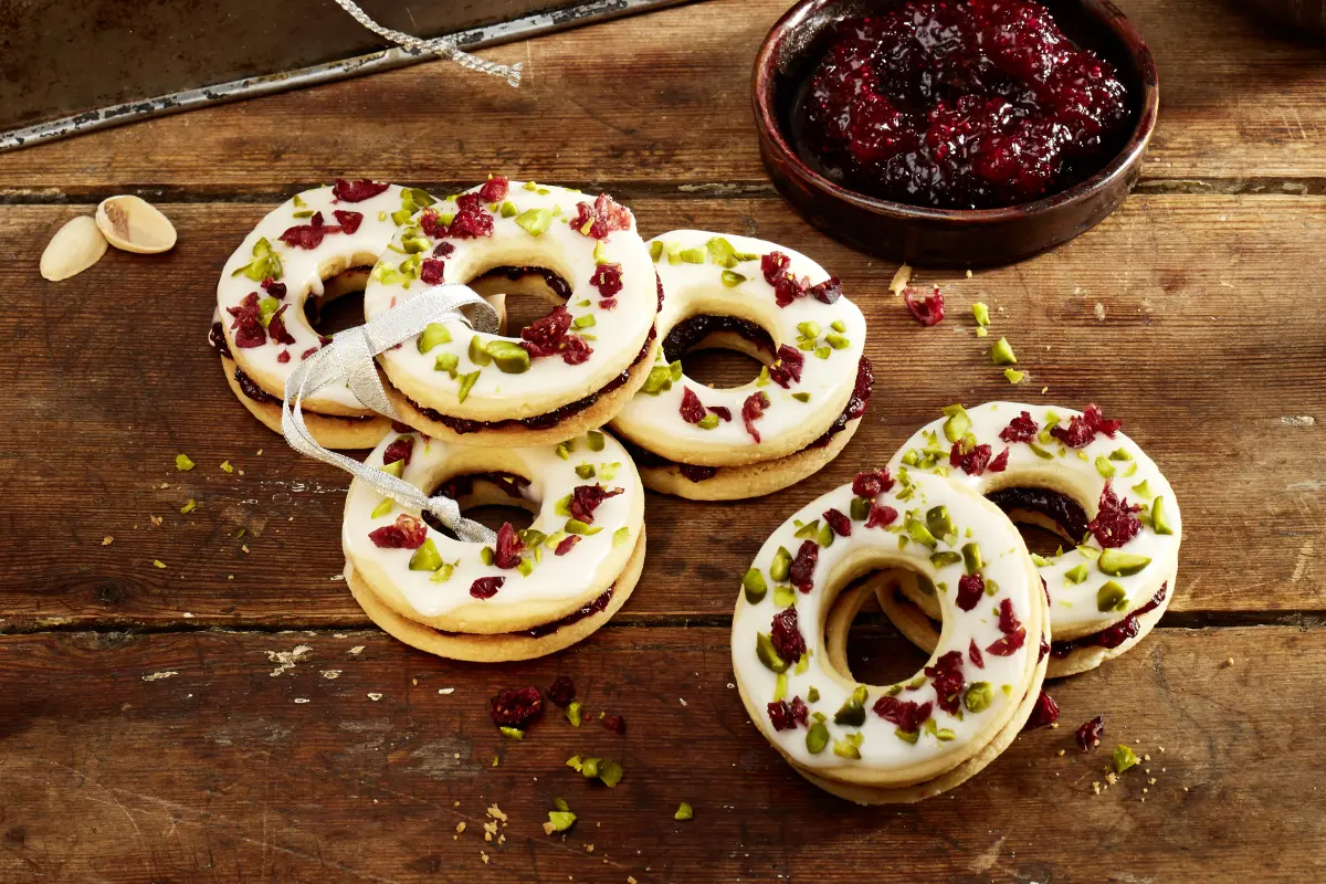 Cranberry-Adventskringel Mehrere Cranberry-Adventskringel auf Holzbrett. Daneben Schüsselchen mit Cranbeery-Konfitüre.