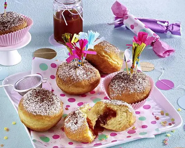Cappuccino-Krapfen mit Hagebutten-Konfitüre Krapfen mit Hagebuttenfuellung mit Cappuccinopulver bestaeubt liegen auf einem Tablett.