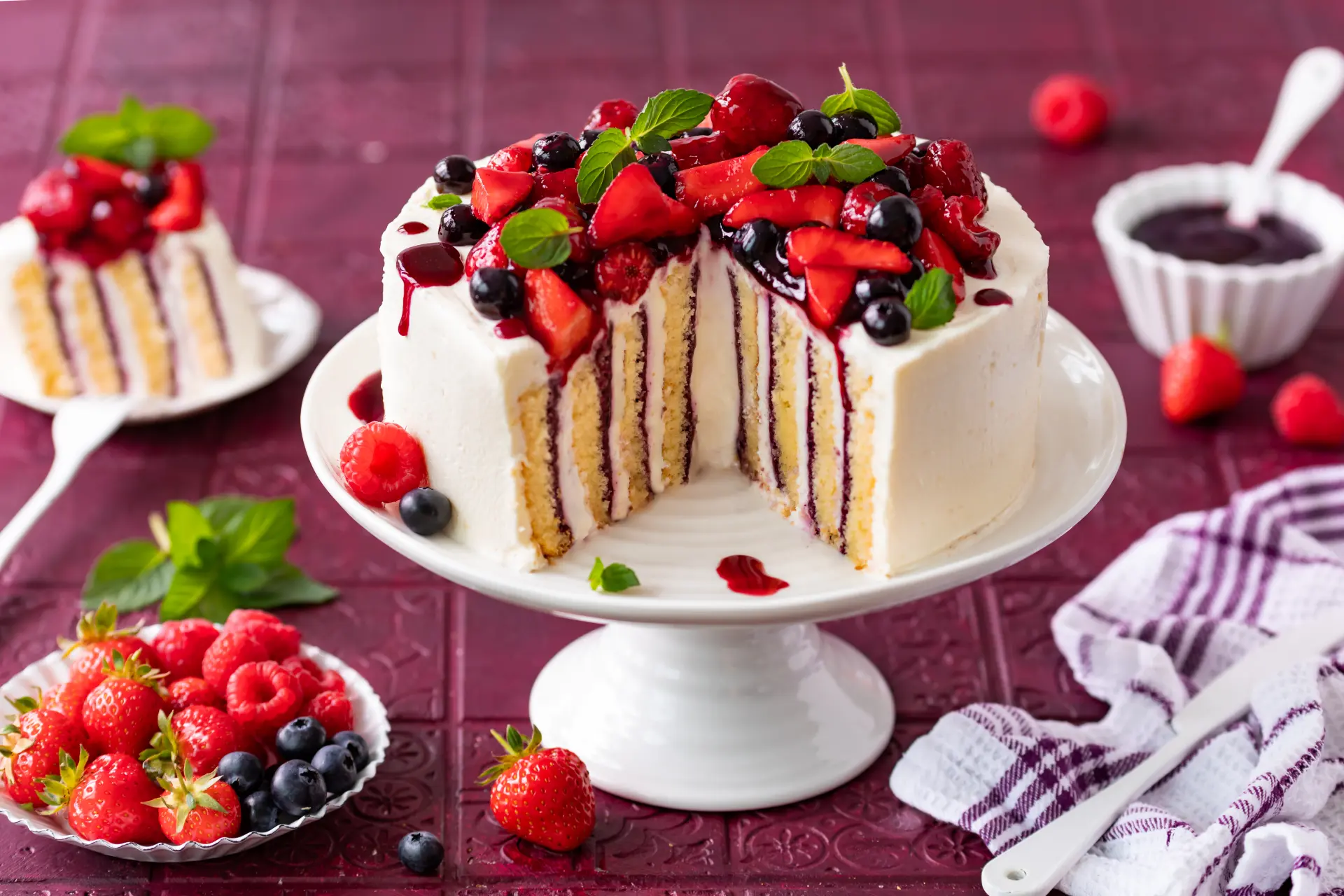 Beeren-Wickeltorte mit Waldfrucht-Fruchtaufstrich Aufgeschnittene Wickeltorte mit heller Cremefüllung, Waldfrucht-Fruchtaufstrich und frischen Beeren auf einer weißen Tortenplatte