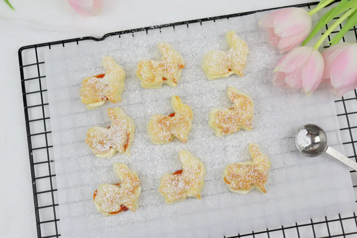 Gefüllte Blätterteighasen mit Buttercreme und Hagebutten-Konfituere auf Backpapier und Gitterrost.
