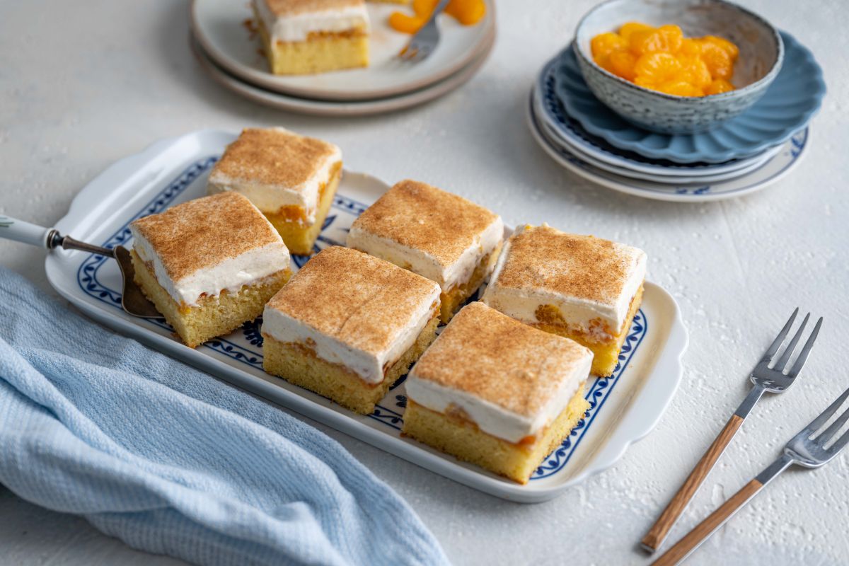 Serviervorschlag Blechkuchen mit Schmand-Sahne-Creme auf Tortenplatte, Tellern, Gabeln, Schüssel mit Mandarinen.